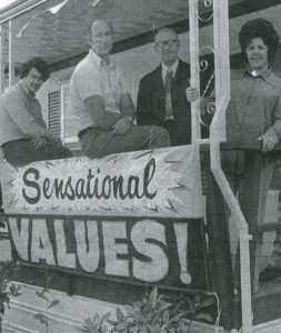 A black and white historical image of Coach Corral's staff behind a banner that reads "Sensational Values!"