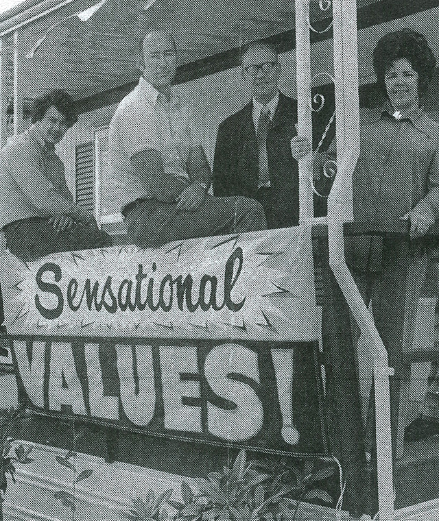 A black and white historic image of Coach Corral's staff behind a banner that reads 'Sensational Values!'